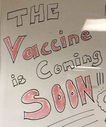 Dry erase board with slogan "the vaccine is coming soon" photo